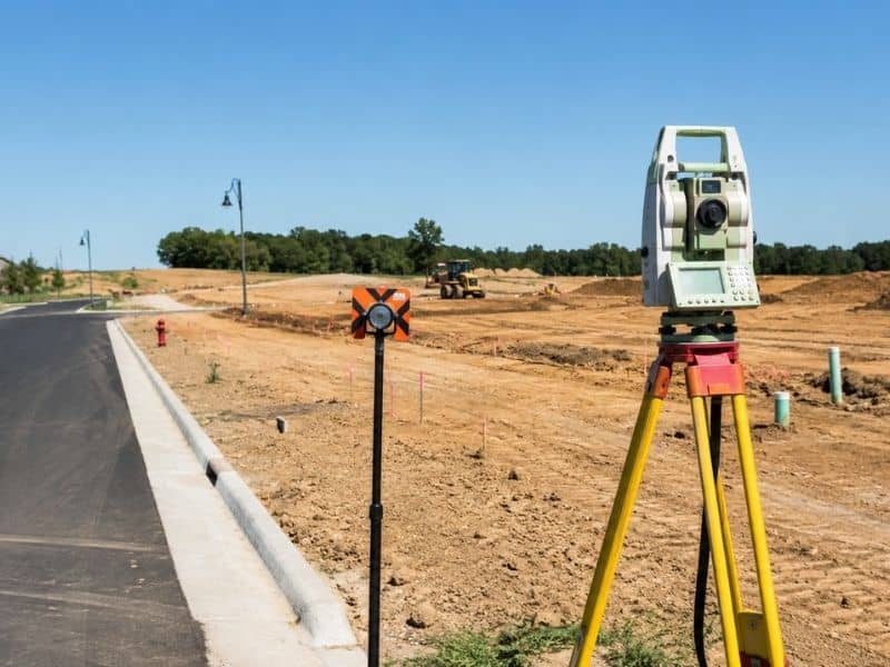 Survey equipment establishing construction control where a new subdivision road extends beyond an existing paved street.