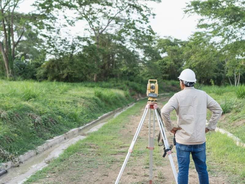 Surveyor evaluating terrain and drainage features on rural land before purchase near Clarksville.