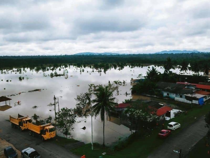 Aerial view of a flooded residential area with submerged houses and roads showing water spread across low elevation terrain highlighting flood impact zones.
